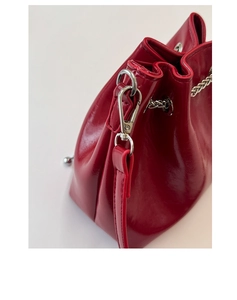 Détail d'un sac seau rouge verni avec chaîne en argent poli et fermoir métallique