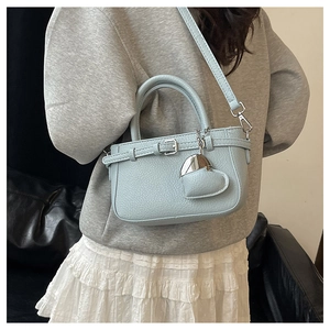 Back view of a light blue lychee pattern crossbody bag with heart charm on a model