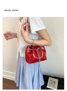 Detail view of red glossy patent leather bucket bag with metal chain drawstring on a model