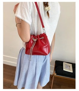 Sac seau rouge avec cordon chaîne porté par un mannequin dans un décor minimaliste