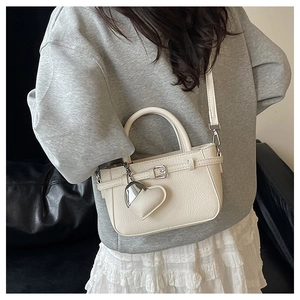 Detail of lychee textured cream mini crossbody bag featuring heart pendant and metal buckle