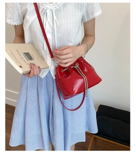 Detail of red patent leather bucket bag with silver chain drawstring on a model