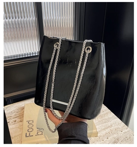 Detail of glossy black bucket bag with vintage wrinkled texture and silver chain straps