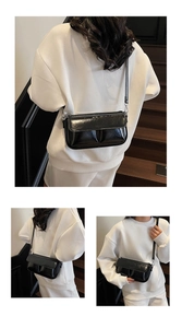 Detail of black glossy crossbody bag showing textured bottom folds and metallic buckles