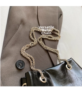 Detail of silver metal chain strap and glossy black pleated leather on a bucket bag