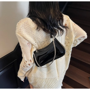 Détail d'un sac sous le bras en cuir verni noir avec chaîne argentée porté par un modèle