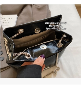 Detail view of glossy black bucket bag with silver chain strap and magnetic closure