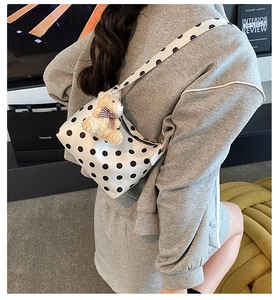 Close-up of white polka dot shoulder bag featuring a cute brown plush bear charm