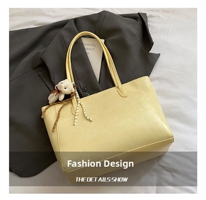 Détail du cabas jaune clair avec motif crocodile, breloque d'ours blanc et poignées solides