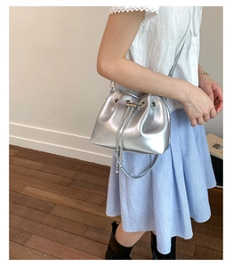 Silver metallic bucket bag with drawstring and chain strap shown on model outdoors