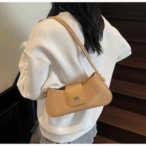Sac baguette chic en cuir verni marron clair porté sous le bras avec logo métallique