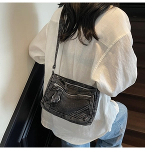 Detail of washed black denim crossbody bag with multiple zippers and decorative tassels