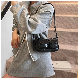 Detail of minimalist black glossy shoulder bag featuring dual front pockets and thin straps