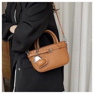Brown lychee leather handbag with heart pendant shown on model's shoulder in black blazer
