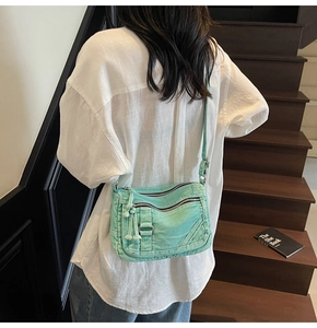 Detail of mint green washed denim crossbody bag with dual stitching and multiple zippers