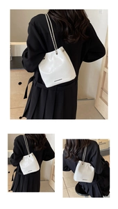 Detailed view of a white glossy leather bucket bag featuring a silver metal bar and chain strap