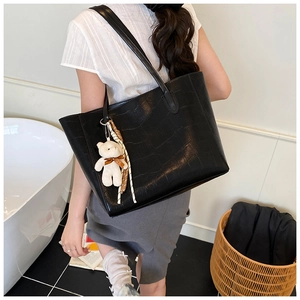 Close-up of black crocodile pattern tote bag with teddy bear and checkered scarf detail