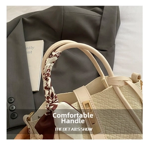Detail of cream woven bucket bag with gold buckle and silk scarf handle accent