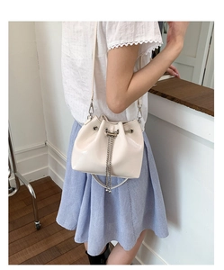 Close-up of cream white bucket bag with silver chain drawstring and glossy finish