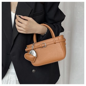 Close-up of brown pebbled leather handbag with buckle detail and heart charm