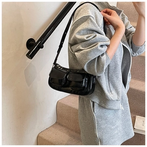 Close-up of black patent leather shoulder bag with two flap pockets and slim strap