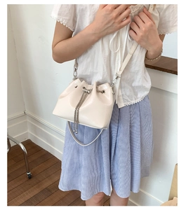 Close-up of a cream white bucket bag featuring silver chain drawstring and glossy finish