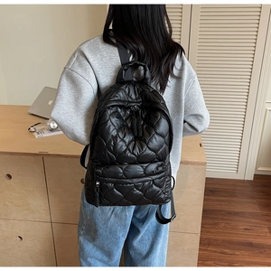 Detail of black quilted backpack with woven rope zipper on a model in a casual setting