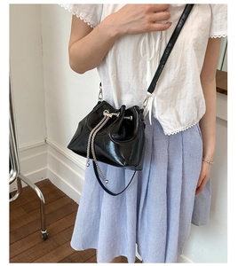 Détail d'un sac seau noir brillant avec chaîne argentée et cordon de serrage sur modèle