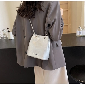 Detail of silver bucket bag with metallic texture, fine chain strap and drawstring closure