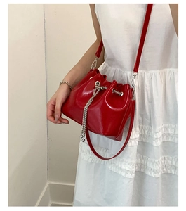 Détail d'un sac seau en cuir verni rouge avec chaîne argentée et bandoulière en cuir