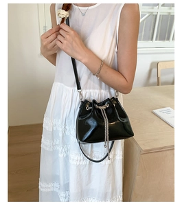 Détail d'un sac seau en cuir verni noir avec cordon de serrage en chaîne métallique