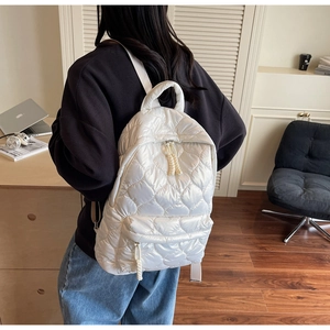 Detailed back view of white quilted nylon backpack worn by model in home office setting