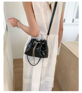 Détail du sac seau en cuir verni noir avec chaîne argentée et fermeture par cordon