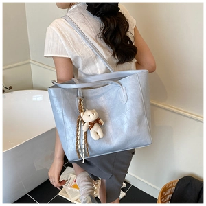 Detailed back view of a light blue crocodile pattern tote bag with a cute bear charm