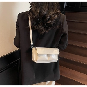 Detail of cream glossy baguette bag with front pockets and silver hooks on black blazer