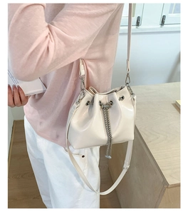 Détail d'un sac seau crème avec chaîne argentée et bandoulière en cuir porté par mannequin