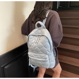 Detail of light blue quilted nylon backpack with large diamond patterns and woven zipper