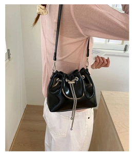 Detail of glossy black bucket bag featuring silver chain tassels and drawstring closure