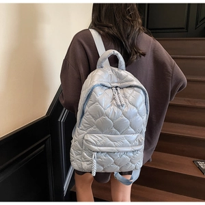 Detail of silver blue quilted backpack showing high-shine fabric and embroidery on stairs