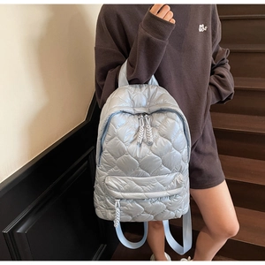 Detail of light blue quilted backpack showing diamond stitching and woven zipper pull