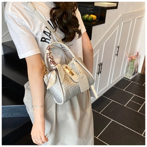 Close-up of woven bucket bag with gold lock and decorative silk scarf on handle