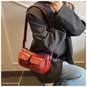 Detail view of red patent leather shoulder bag with symmetrical flap pockets and silver hardware