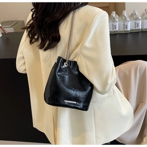 Detail of black leather bucket bag with silver chain strap on a model shoulder