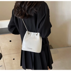Detail of white glossy leather bucket bag with silver chain strap and metal trim