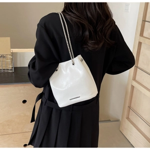 Close-up of a white leather bucket bag with silver chain strap worn by a model