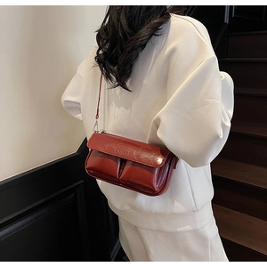 Detail of burgundy glossy leather crossbody bag with pleated design worn by a model