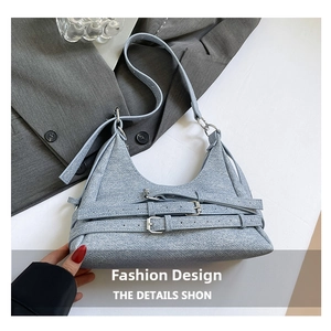 Détail du sac croissant en denim bleu clair avec boucles métalliques de style motard