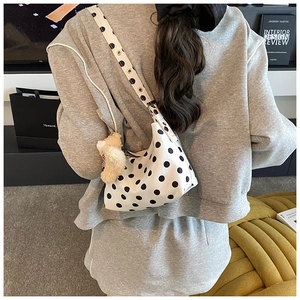 Detail view of white spotted shoulder bag with metal eyelet strap and plush bear charm