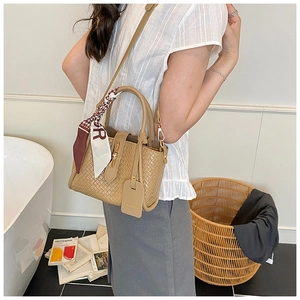 Detail of woven khaki bucket bag featuring decorative silk scarf on handle and shoulder strap