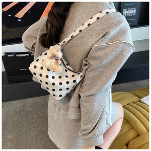 Detail of white polka dot shoulder bag featuring a cute brown plush bear charm and zip closure